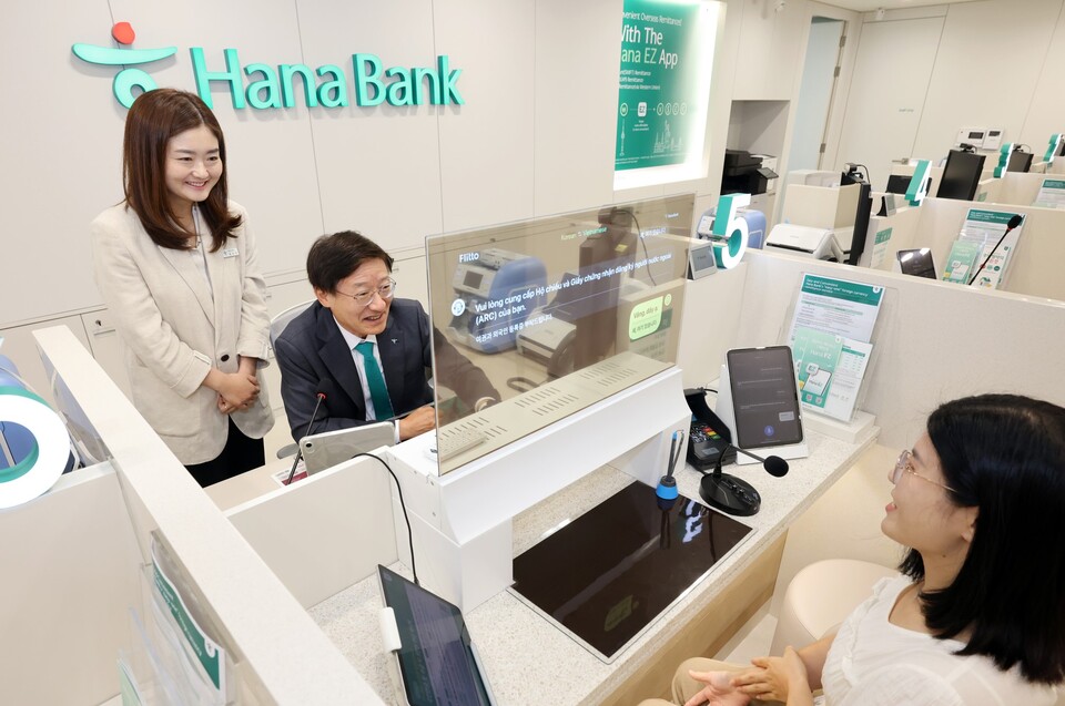 하나은행은 19일 경기도 평택시 평택동에 소재한 외국인 전용 특화점포 '평택외국인센터점'을 개점했다. 이승열 하나은행장(사진 가운데)이 실시간 다국어 통번역 시스템이 설치된 창구에 앉아 투명디스플레이를 통해 외국인 손님을 응대하고 있다. [하나은행 제공]