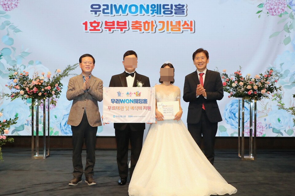 지난 13일 취약계층 신혼부부의 결혼식을 위해 우리금융 본사 사옥 웨딩홀을 무료로 대관해 주는 '우리 WON 웨딩홀' 1호 부부가 탄생했다. (왼쪽부터) 조병규 우리은행장, '우리 WON 웨딩홀' 1호 부부, 김현훈 서울특별시사회복지협의회장이 기념촬영을 하고 있다. [우리은행 제공]