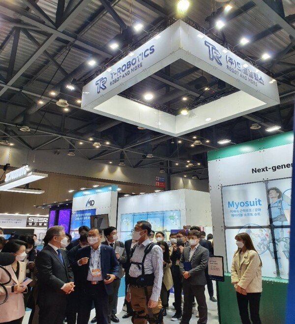 이재명 대통령(사진 왼쪽 파란 넥타이 인물)이 대선 후보 시절, 한 박람회에서 티로보틱스의 마이요슈트에 대한 설명을 듣고 있다. [사진=티로보틱스]